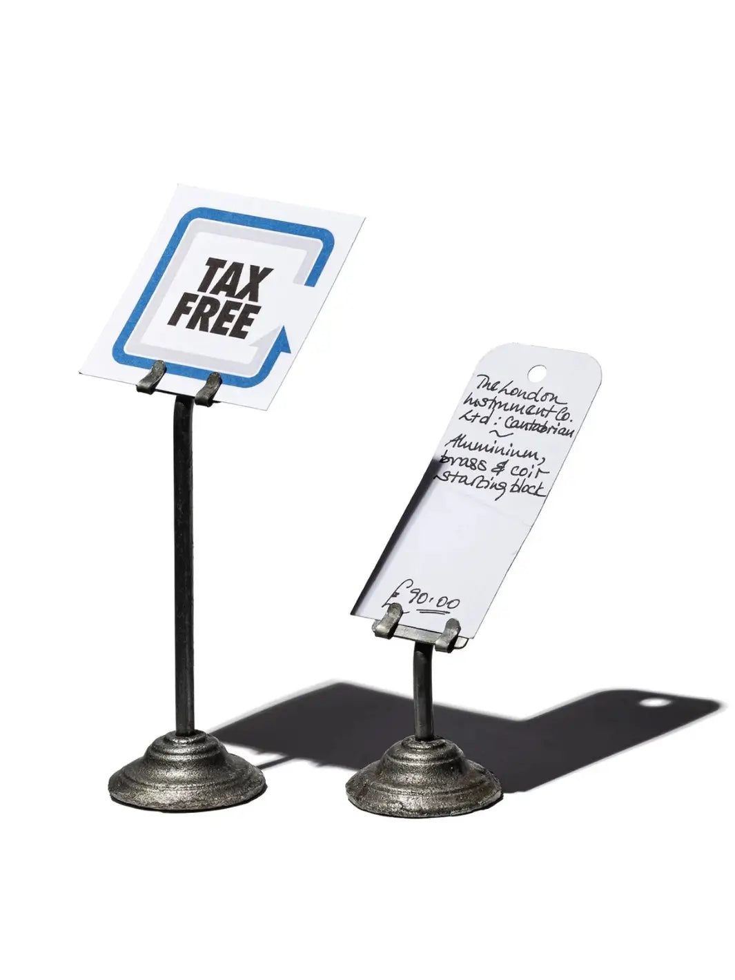 Industrial-style Card Holder / H120 from Puebco stands of varying heights are shown holding a "Tax Free" sign and a handwritten price tag | Twentyseven Toronto