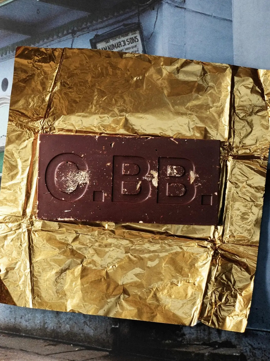 A dark Cardamom Chocolate Bar from Casa Bosques featuring large embossed lettering and small square details, resting inside its opened gold foil wrapper | Twentyseven Toronto
