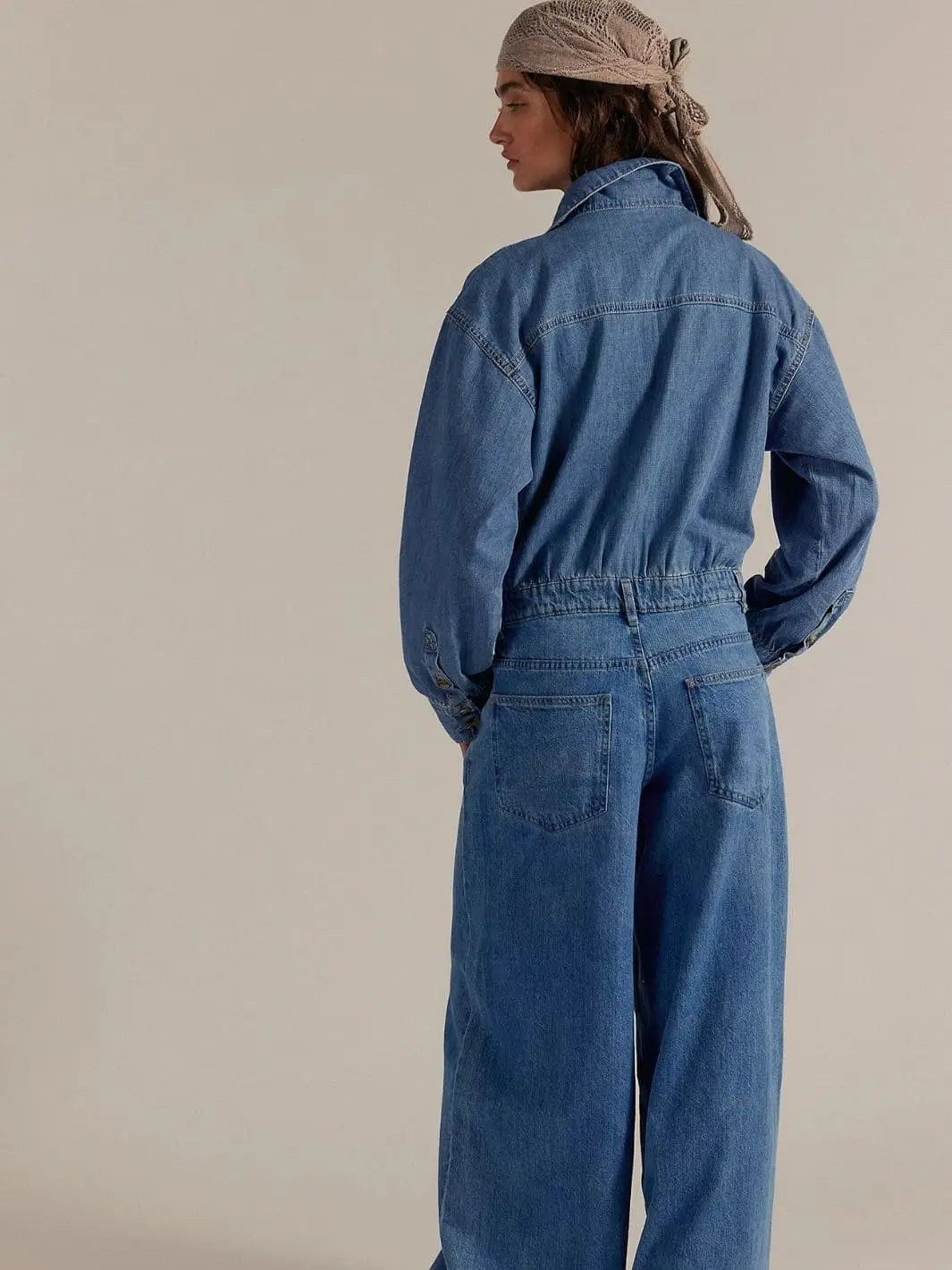 A rear view showcases the back pockets and slouchy fit of the denim Free People Carpe Diem One-Piece in New Day | Twentyseven Toronto