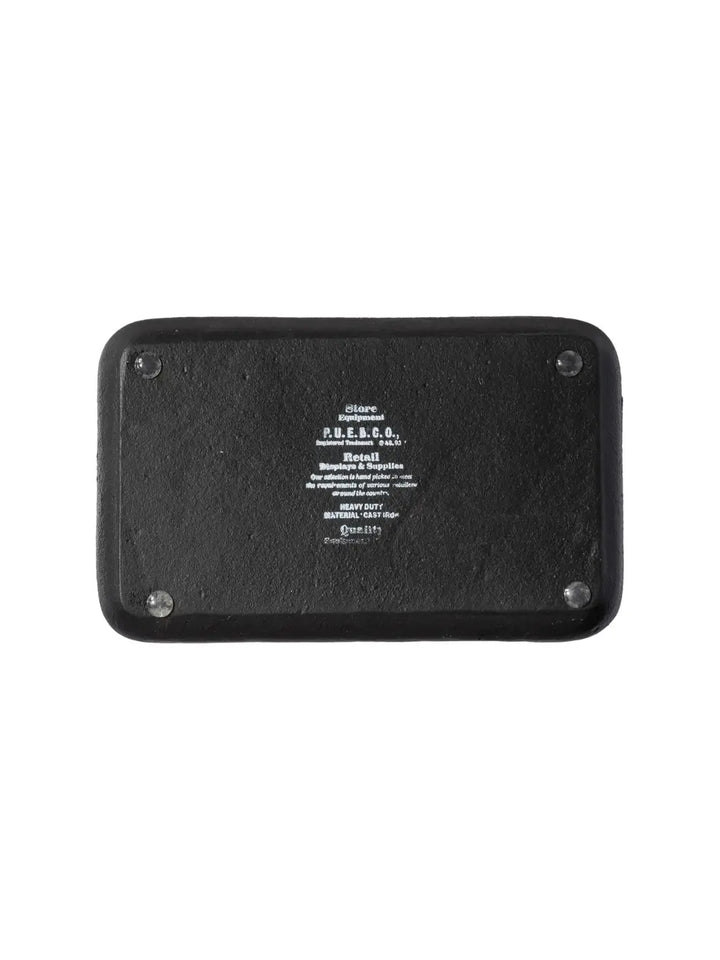 The underside of the Cast Iron Tray - Black from Puebco detailed with embossed branding text reading "P.U.E.B.C.O. Heavy Duty Material Cast Iron" and four small, protective rubber feet on the corners | Twentyseven Toronto