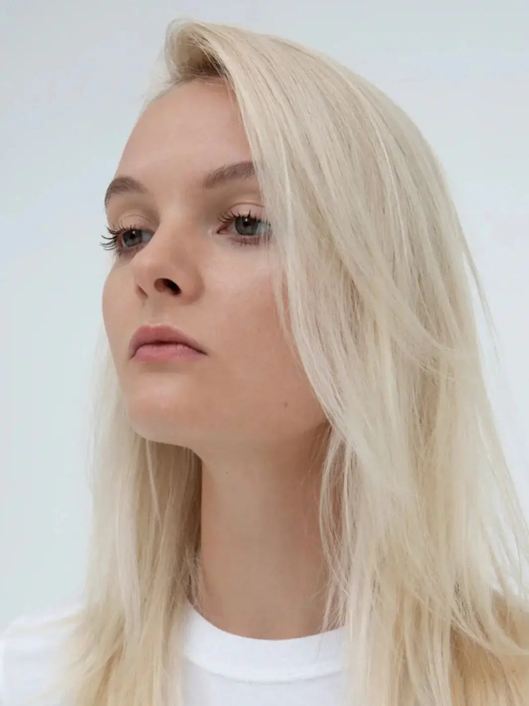 A side-profile headshot of a model showcasing smooth, healthy-looking blonde hair styled with R+Co CENTERPIECE All-In-One Elixir Spray | Twentyseven Toronto