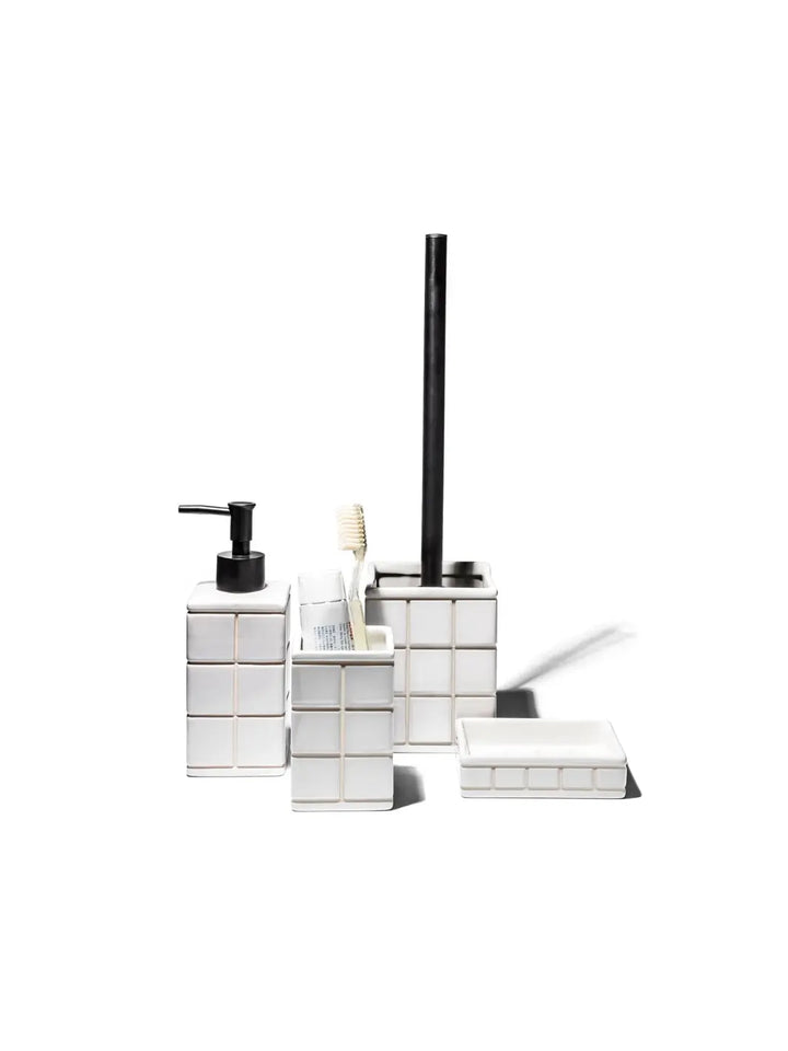 A collection of white tiled bathroom items, including a liquid soap pump, a toothbrush holder, a toilet brush holder, and the Ceramic Bath Ensemble / Soap Dish from Puebco against a white background | Twentyseven Toronto