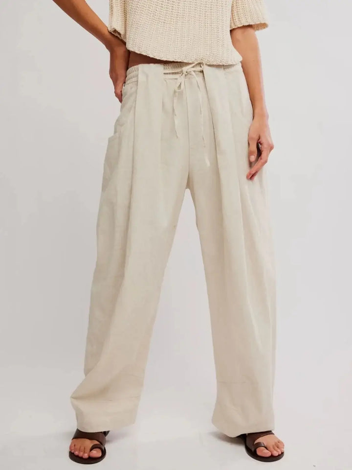 A full-length studio shot displays the loose, wide-leg drape of the Free People Chambers Laidback Pull-On Pants in Summer Sand paired with a cream knit top and brown leather sandals | Twentyseven Toronto