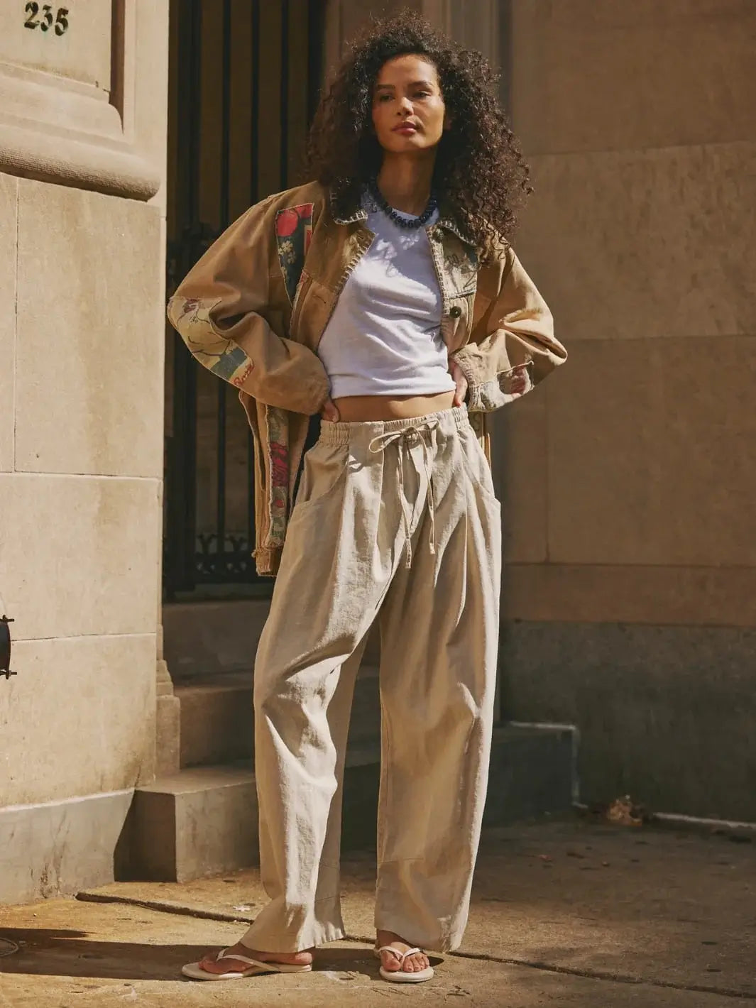 A full-length outdoor image showcases a model posing with hands on hips to exhibit the slouchy volume and low-slung potential of the Free People Chambers Laidback Pull-On Pants in Summer Sand | Twentyseven Toronto