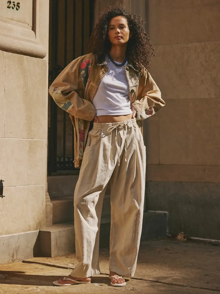 A full-length outdoor image showcases a model posing with hands on hips to exhibit the slouchy volume and low-slung potential of the Free People Chambers Laidback Pull-On Pants in Summer Sand | Twentyseven Toronto