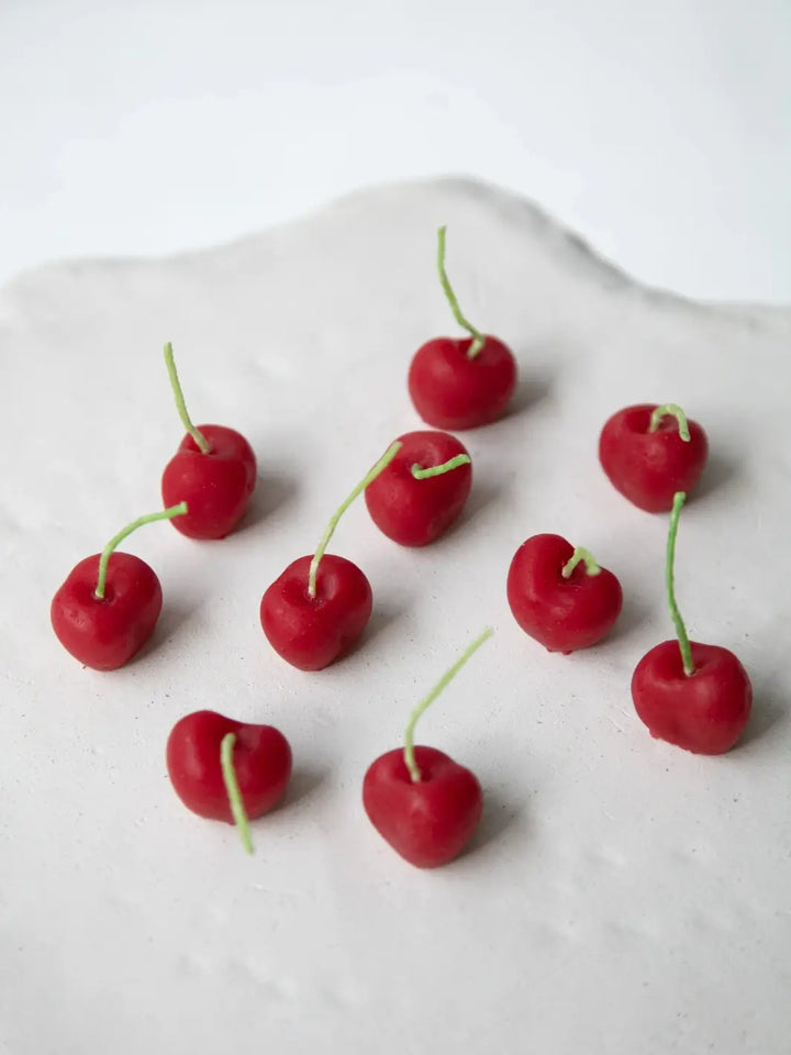 Set of 10 red cherry-shaped beeswax candles from Happy Organics on a white table | Twentyseven Toronto