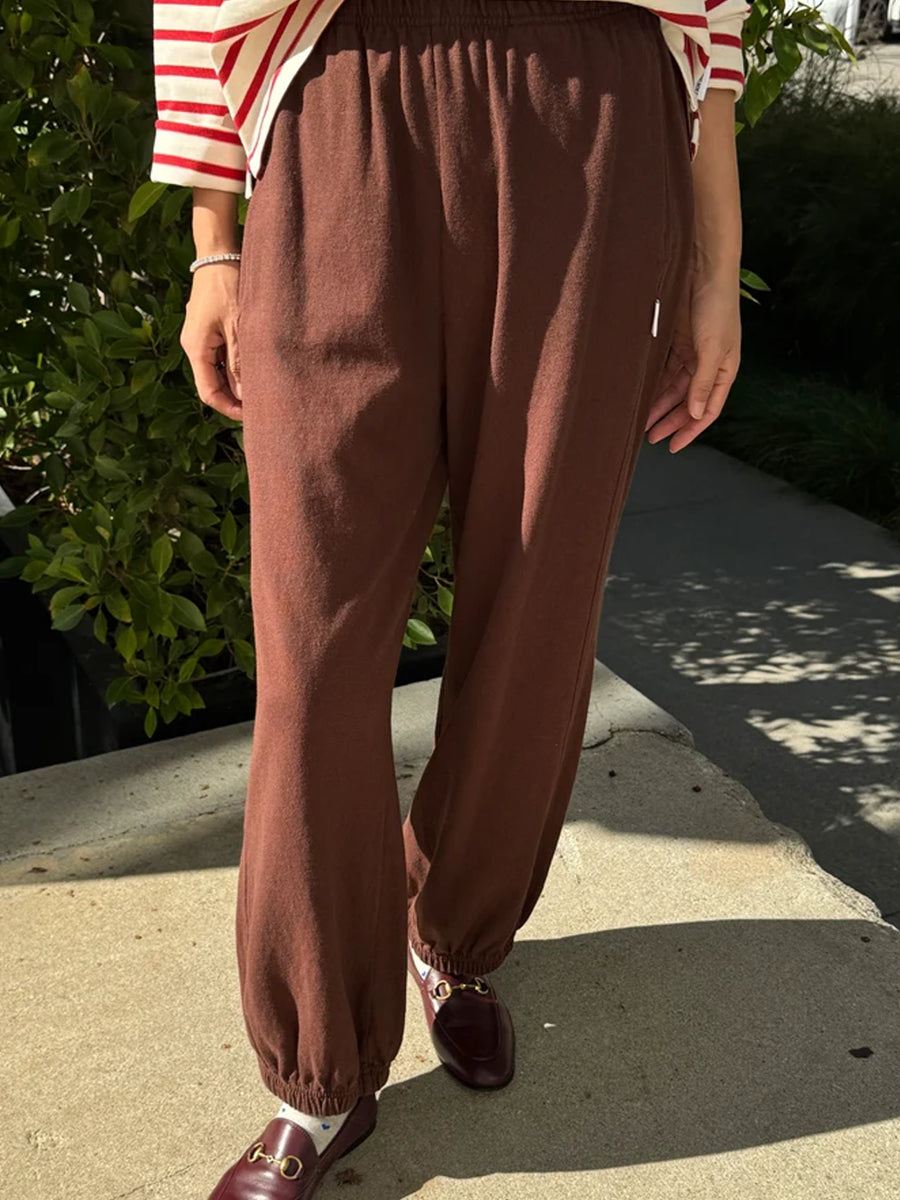 Front view of Chestnut Brown Balloon Pants featuring a relaxed, voluminous fit, elastic waistband and gathered ankle cuffs, styled with a red and cream striped top and burgundy loafers | Twentyseven Toronto