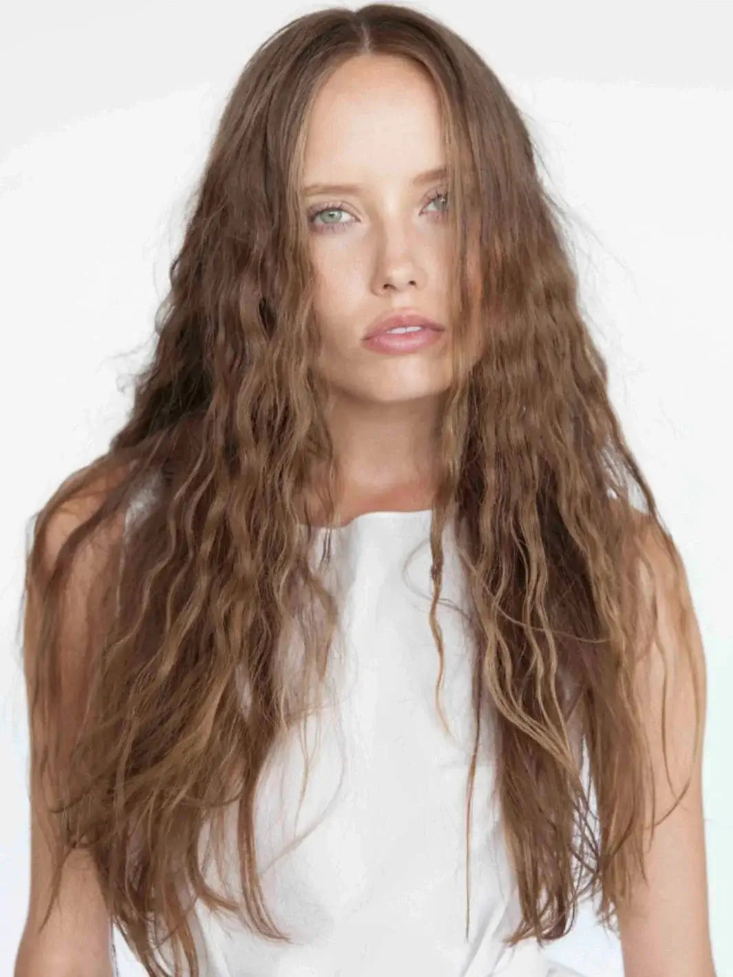 A model with long, wavy brown hair showcases lightweight volume and texture after styling with R+Co CHIFFON Styling Mousse | Twentyseven Toronto