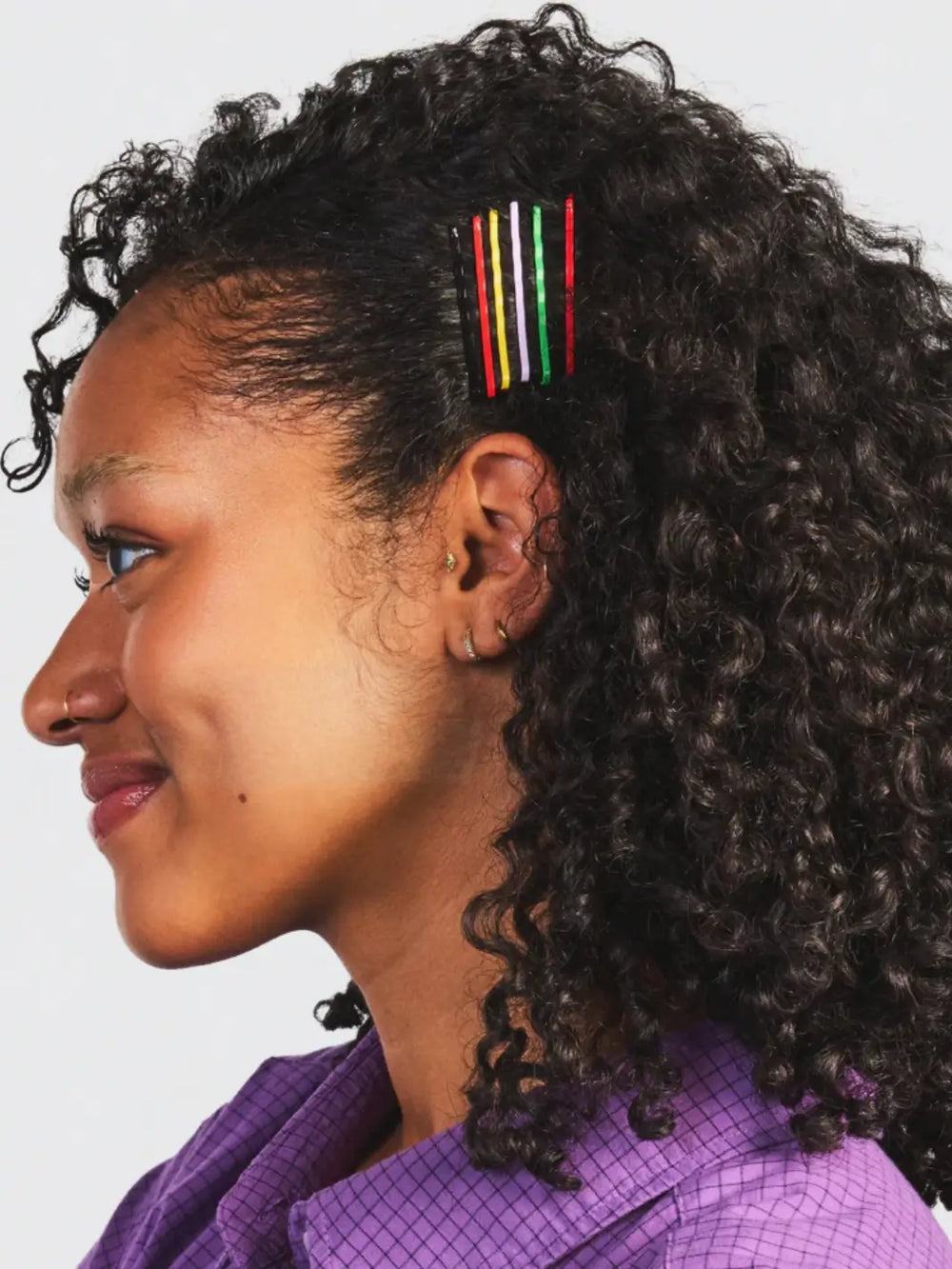 A side profile shot of a person with curly dark hair wearing a neat row of five multi-colored Chunks Hairclips Chunks Bobby Pins pinned back above their ear | Twentyseven Toronto
