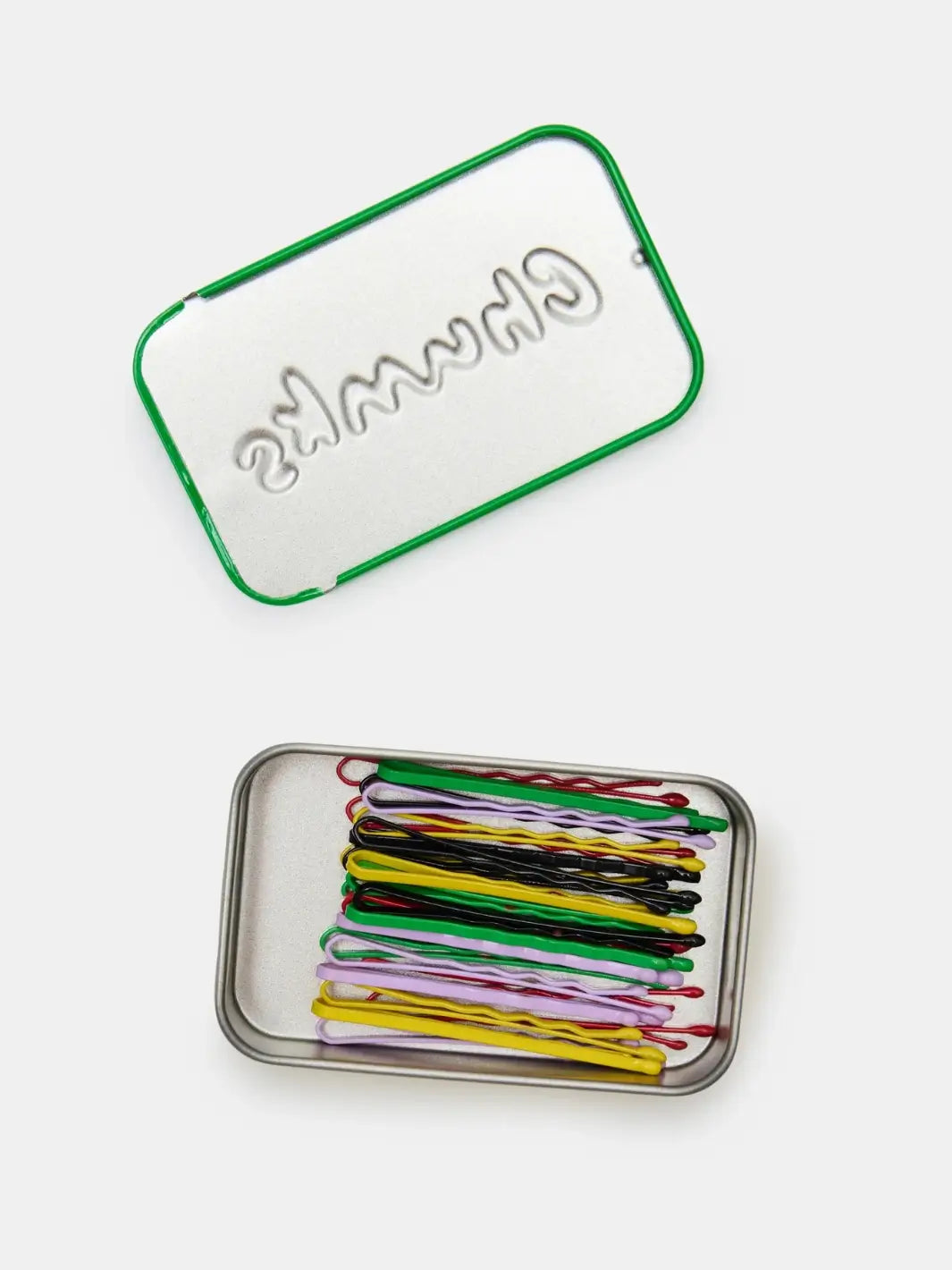 An open metal storage tin viewed from above shows a variety of colorful Chunks Hairclips Chunks Bobby Pins neatly stacked inside next to its matching lid | Twentyseven Toronto