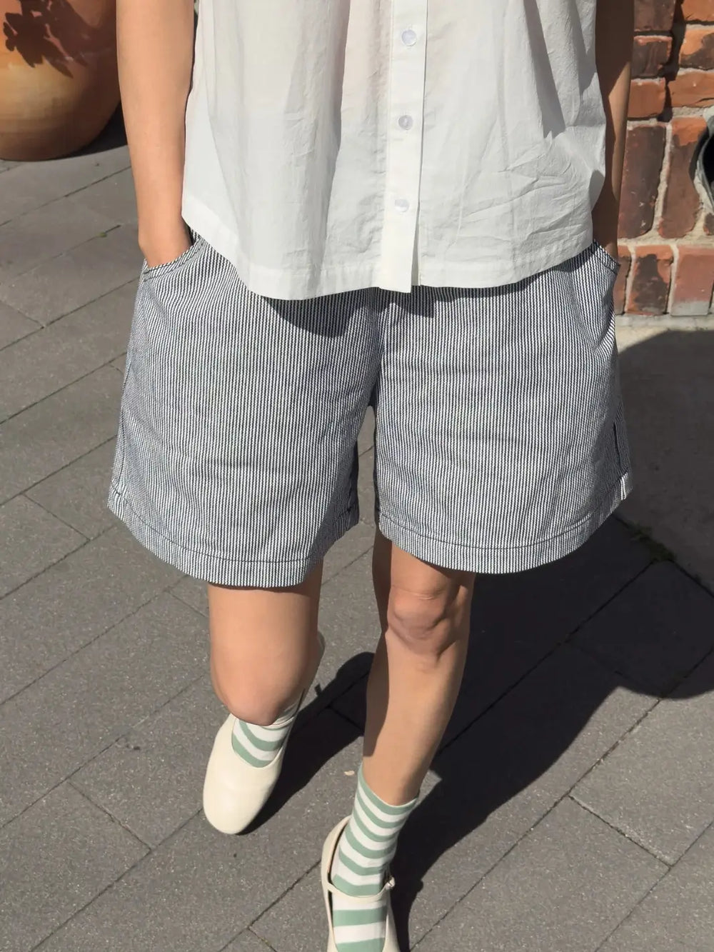 Person wearing a white shirt and white 'City Shorts' in 'Blue Stripe' from Le Bon Shoppe on a sidewalk | Twentyseven Toronto