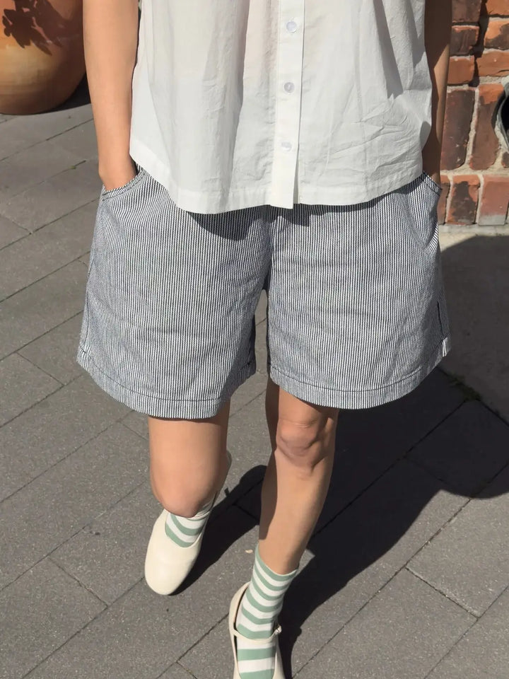 Person wearing a white shirt and white 'City Shorts' in 'Blue Stripe' from Le Bon Shoppe on a sidewalk | Twentyseven Toronto
