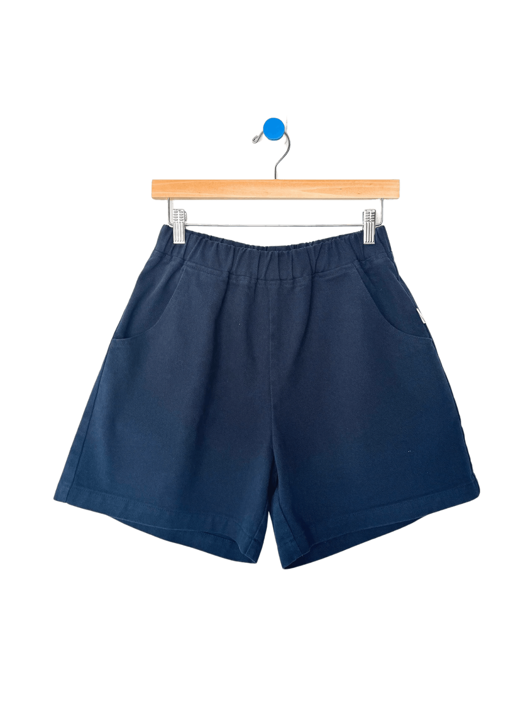 Navy blue 'City Shorts' in 'Navy' from Le Bon Shoppe on a hanger against a transparent background | Twentyseven Toronto