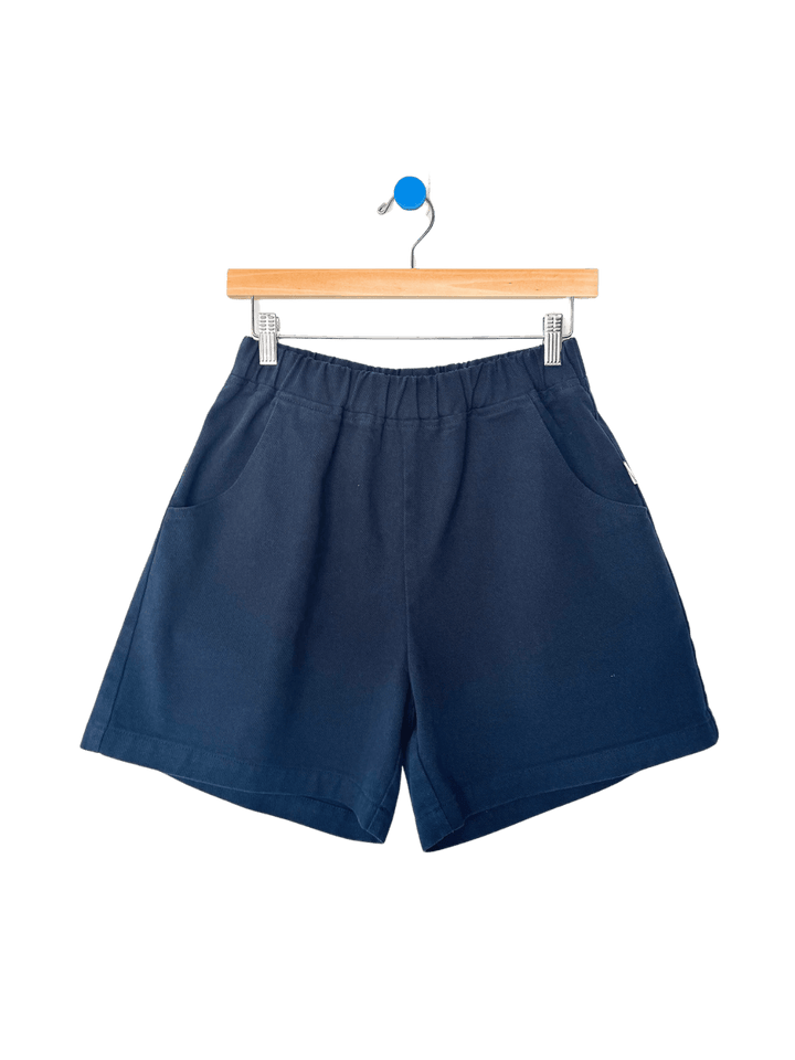 Navy blue 'City Shorts' in 'Navy' from Le Bon Shoppe on a hanger against a transparent background | Twentyseven Toronto