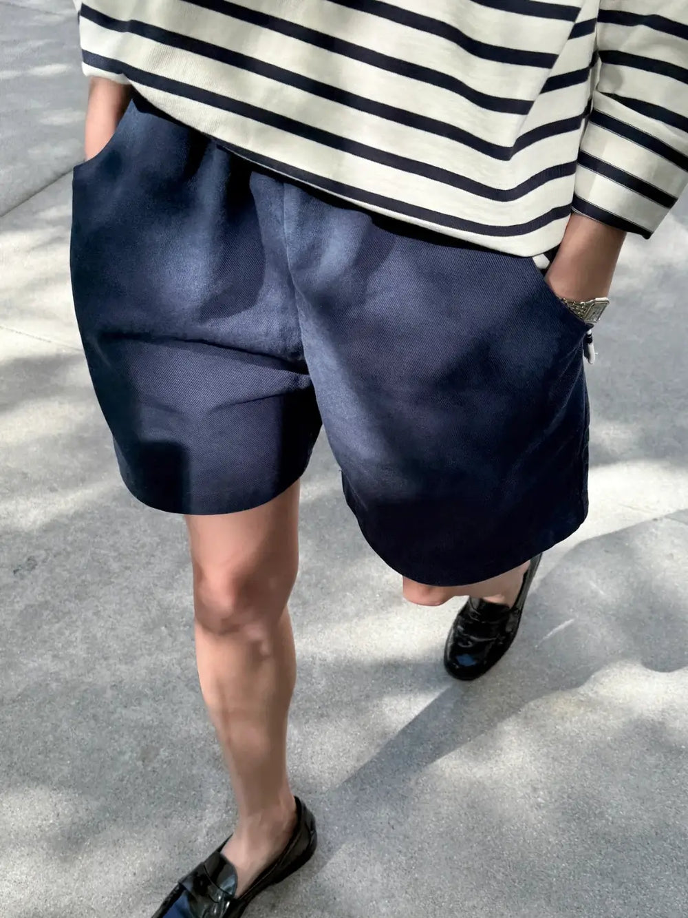 Person wearing navy 'City Shorts' and a striped shirt from Le Bon Shoppe on a concrete surface | Twentyseven Toronto