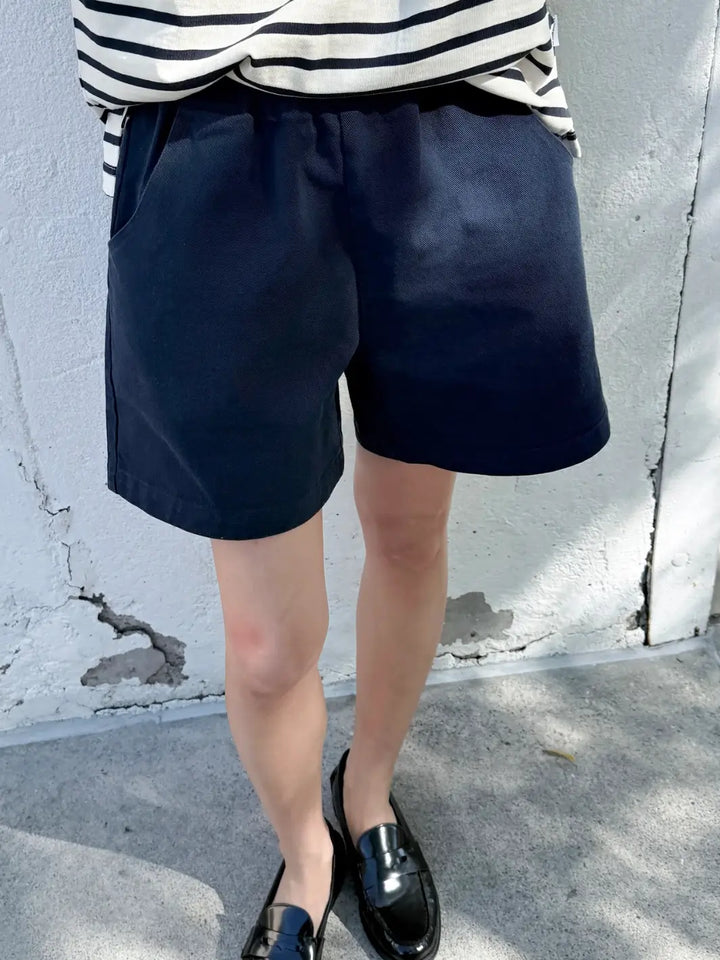 Person wearing navy 'City Shorts' from Le Bon Shoppe and a striped shirt against a gray wall | Twentyseven Toronto