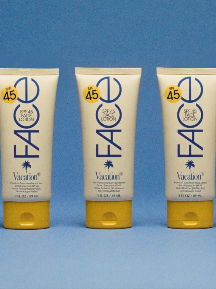 Three identical tubes of Vacation Inc Classic Face Lotion SPF 45 stand upright in a neat row against a textured blue background | Twentyseven Toronto