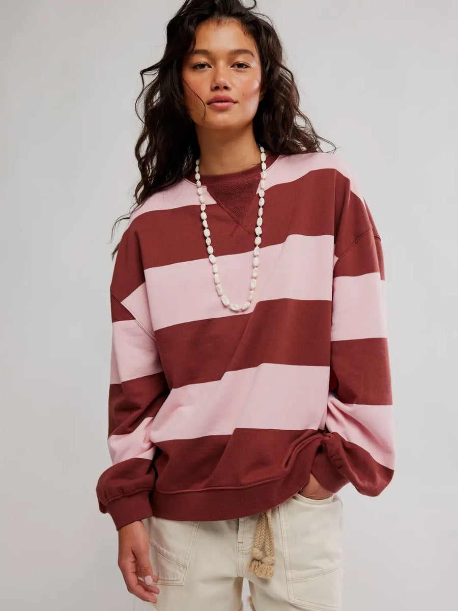 A woman wearing a long white bead necklace and an oversized, pink and burgundy striped pullover top known as the Free People Classic Stripe Crew Wide in Strawberry Wine Combo | Twentyseven Toronto