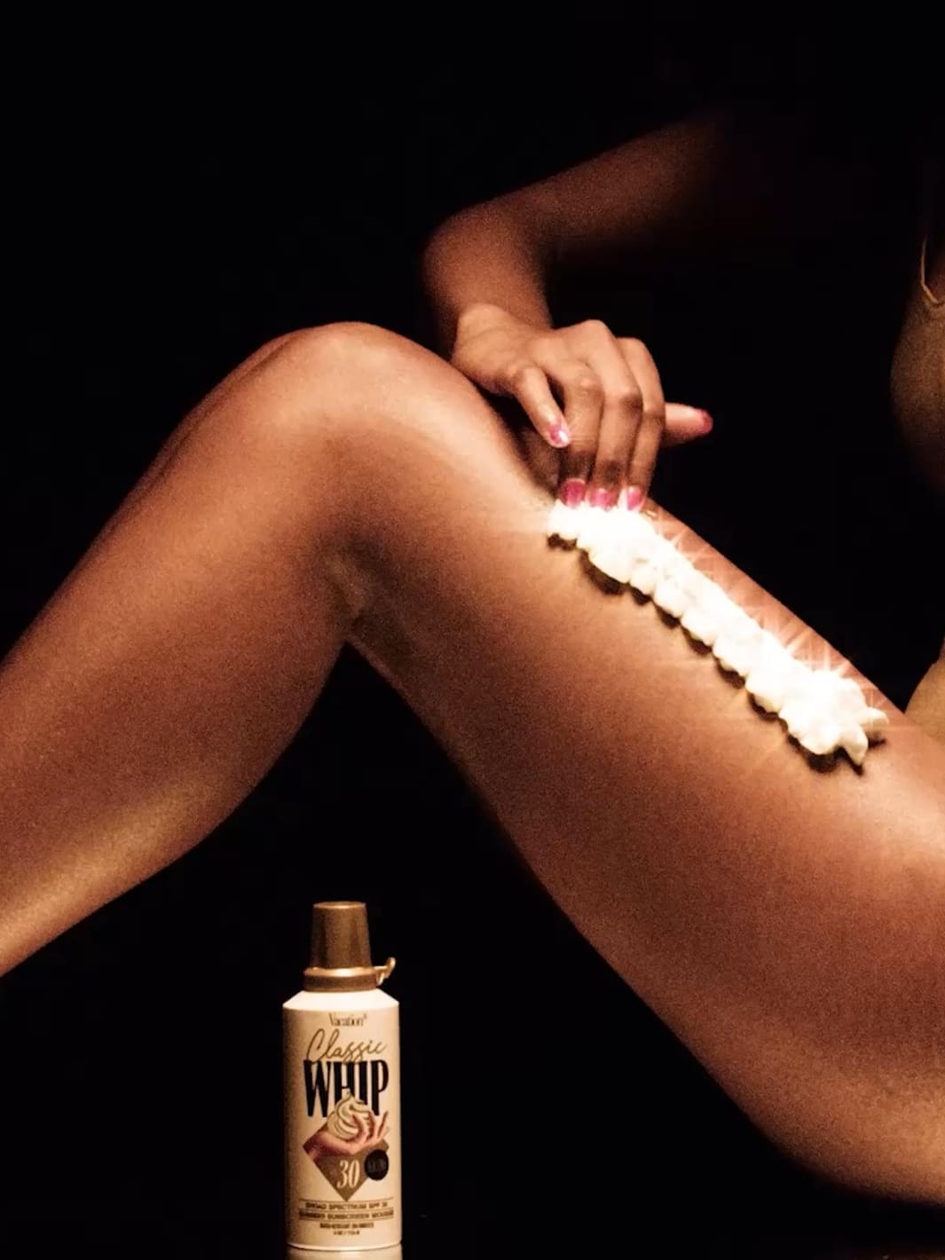 Vacation Inc. Classic Whip Glow SPF 30 | Twentyseven Toronto | Person applying whipped cream to their leg with a can of whipped cream next to them on a black background