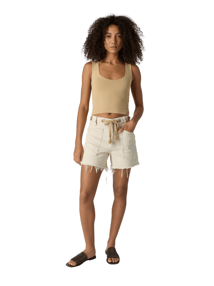 Woman with curly hair wearing a beige 'Clean Lines Muscle Cami' fitted top in 'Oat Latte' from Free People on a transparent background | Twentyseven Toronto