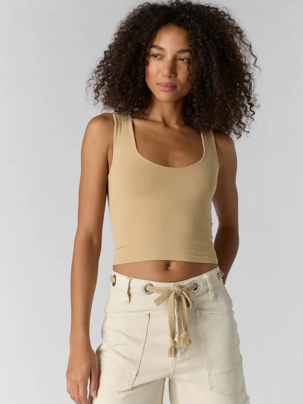 Woman with curly hair wearing a beige 'Clean Lines Muscle Cami' fitted top in 'Oat Latte' from Free People | Twentyseven Toronto