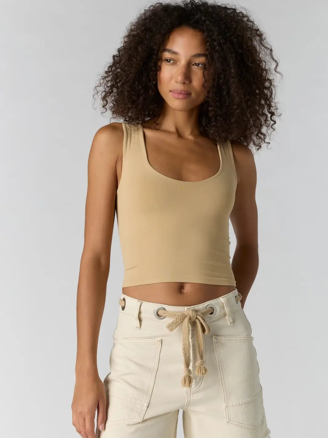 Woman with curly hair wearing a beige 'Clean Lines Muscle Cami' fitted top in 'Oat Latte' from Free People | Twentyseven Toronto