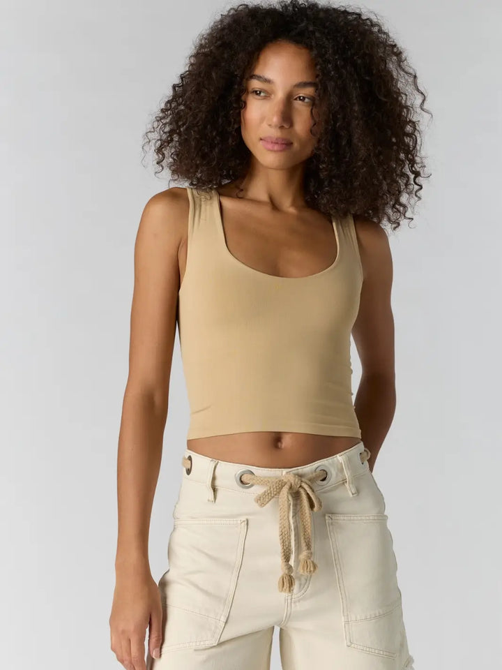 Woman with curly hair wearing a beige 'Clean Lines Muscle Cami' fitted top in 'Oat Latte' from Free People | Twentyseven Toronto