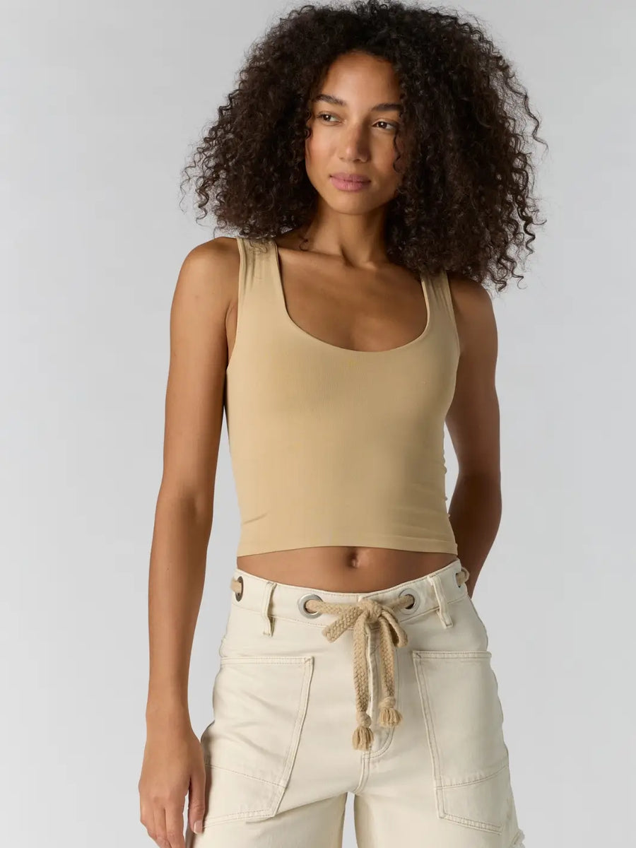 Woman with curly hair wearing a beige 'Clean Lines Muscle Cami' fitted top in 'Oat Latte' from Free People | Twentyseven Toronto