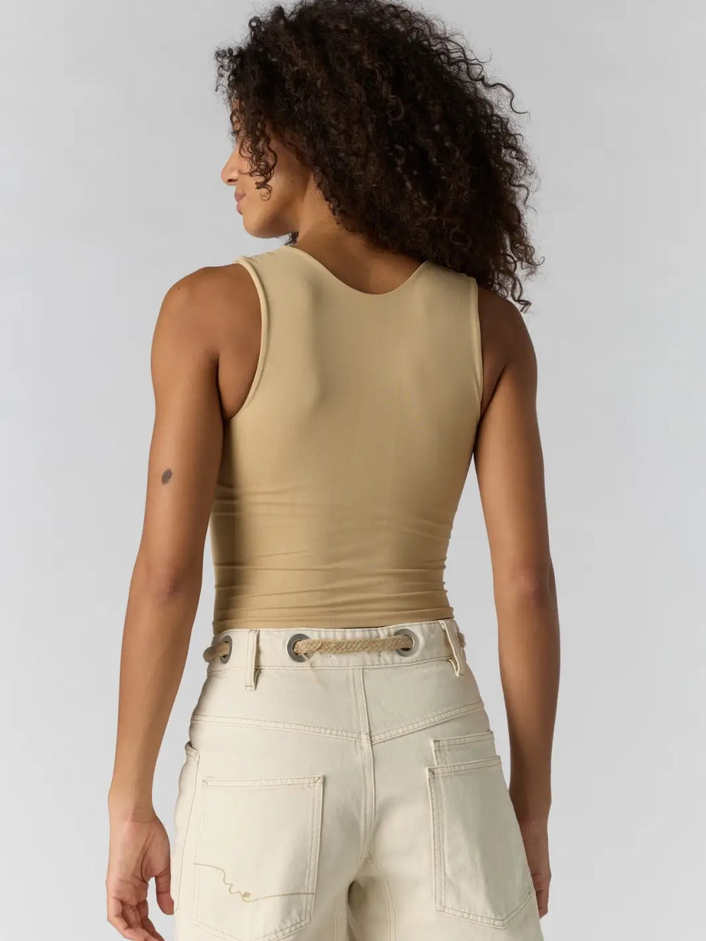 Woman with curly hair wearing a beige 'Clean Lines Muscle Cami' fitted top in 'Oat Latte' from Free People, back view | Twentyseven Toronto
