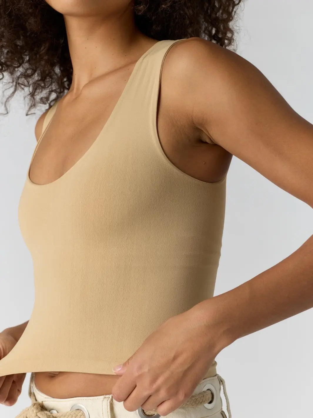 Close up of woman with curly hair wearing a beige 'Clean Lines Muscle Cami' fitted top in 'Oat Latte' from Free People | Twentyseven Toronto