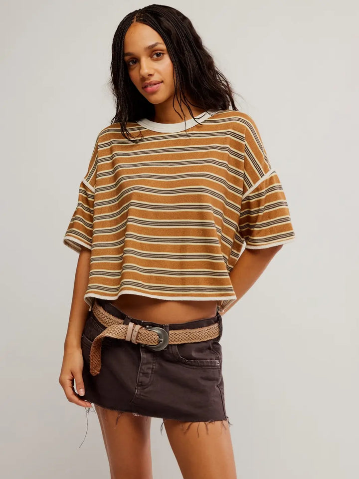 A front view of a model with braided hair wearing the striped, cropped Free People Clean Rugby Tee in Almond Combo paired with a dark denim mini skirt and woven belt | Twentyseven Toronto