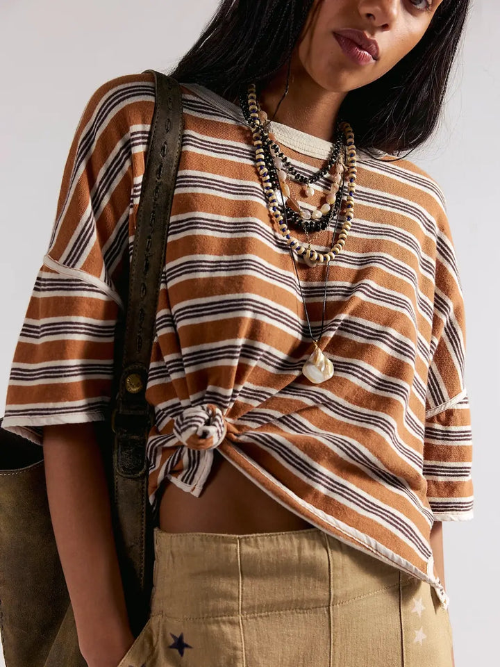 A close-up shot showing a model wearing the Free People Clean Rugby Tee in Almond Combo tied at the side into a knot and accessorized with layered beaded necklaces | Twentyseven Toronto