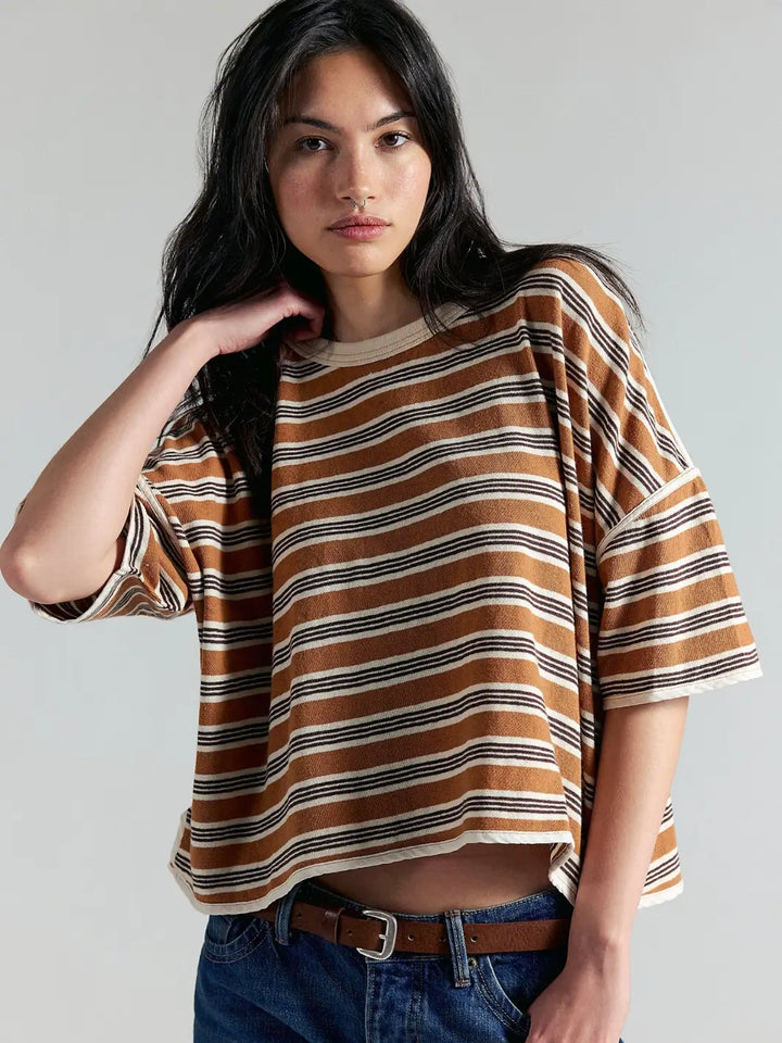 A front medium shot of a model with long dark hair posing in the oversized, horizontally striped Free People Clean Rugby Tee in Almond Combo and blue jeans | Twentyseven Toronto