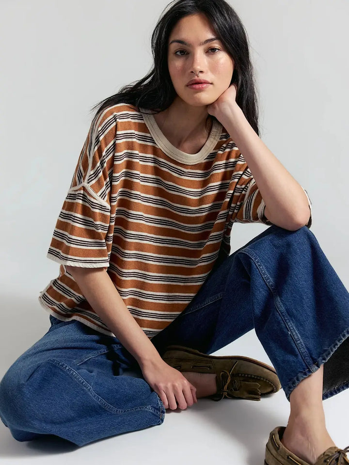 A model sits cross-legged on the floor leaning on her hand while wearing the loose-fitting Free People Clean Rugby Tee in Almond Combo with wide-leg jeans and loafers | Twentyseven Toronto