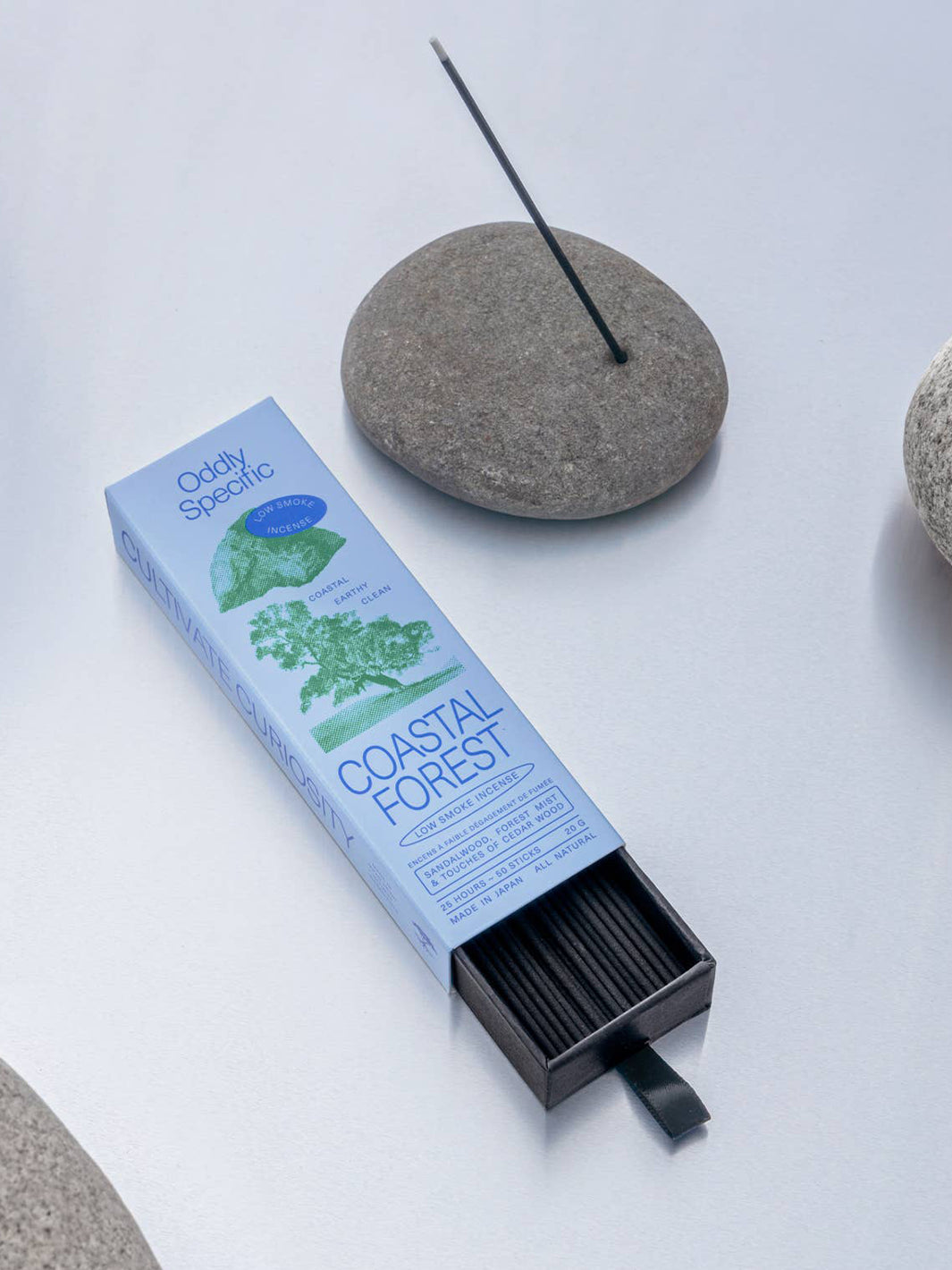Oddly Specific Coastal Forest Japanese incense featuring blue and green packaging, black incense sticks in a pull-out tray and a single incense stick in a grey stone holder | Twentyseven Toronto