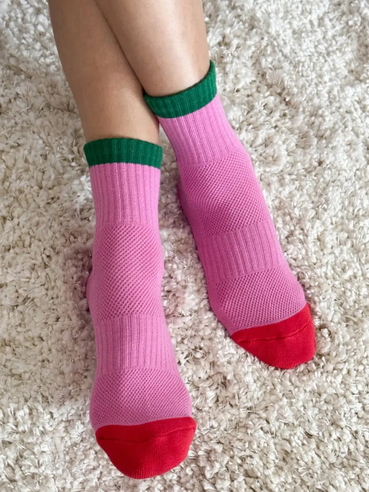 Pink 'Color Block Girlfriend Socks' in 'Rose Green' style from Le Bon Shoppe with red toes and green accents on a bed | Twentyseven Toronto