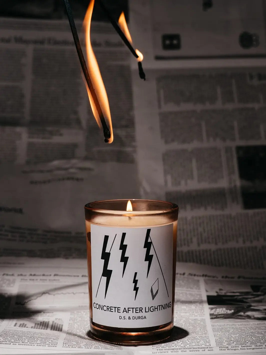 DS&Durga 'Concrete After Lightning' candle with a label featuring lightning bolts on a newspaper background | Twentyseven Toronto