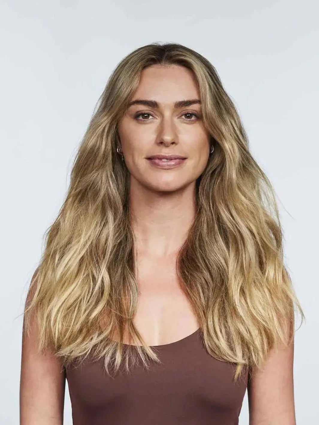 A woman with voluminous, center-parted dirty blonde waves smiles against a white background to showcase the effortless styling from Hair by Sam McKnight Cool Girl Barely There Texture Spray | Twentyseven Toronto