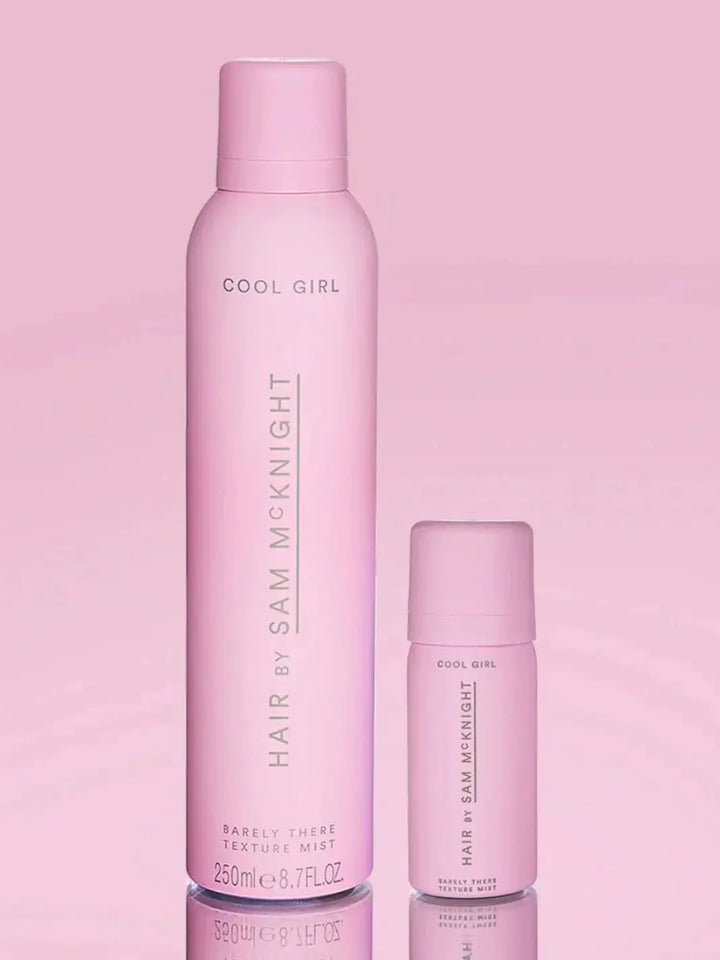 A standard-size aerosol can and a mini travel-size bottle stand side-by-side on a reflective surface to highlight the size options of Hair by Sam McKnight Cool Girl Barely There Texture Spray | Twentyseven Toronto