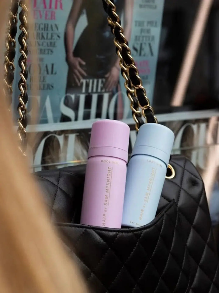 A mini travel-size bottle of Hair by Sam McKnight Cool Girl Barely There Texture Spray tucks neatly into a quilted black leather purse next to a light blue spray can | Twnetyseven Toronto
