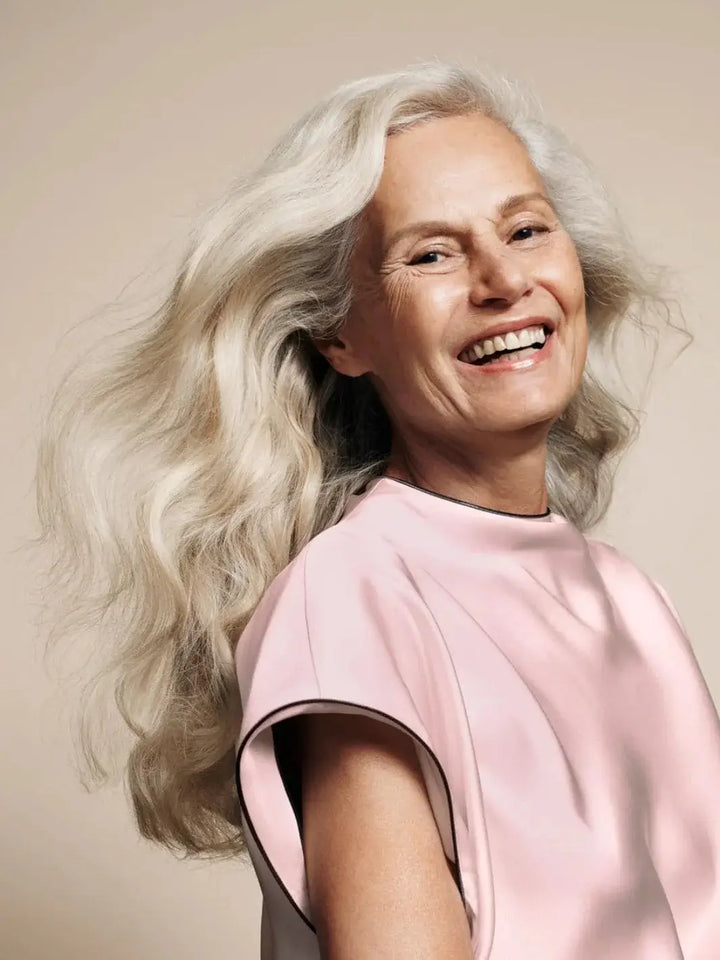 A smiling model showcases her voluminous, thick silver hair flowing naturally after being treated with Hair by Sam McKnight Cool Girl Volume Conditioner | Twentyseven Toronto