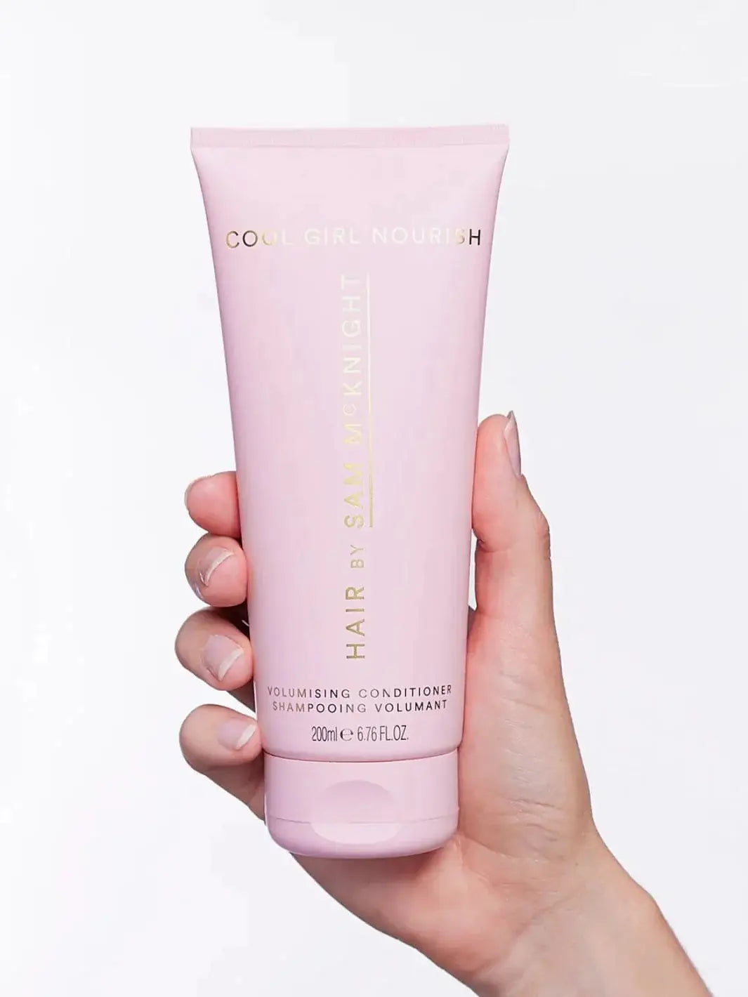 A close-up studio shot highlights the pink tube packaging of the Hair by Sam McKnight Cool Girl Volume Conditioner held against a plain white background | Twentyseven Toronto