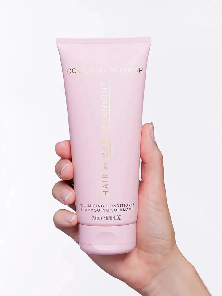 A close-up studio shot highlights the pink tube packaging of the Hair by Sam McKnight Cool Girl Volume Conditioner held against a plain white background | Twentyseven Toronto