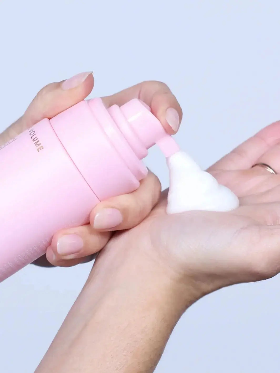 A close-up view shows a dollop of airy, white styling product being pumped out of a pink bottle into a hand to demonstrate the texture of Hair by Sam McKnight Cool Girl Volume Foam | Twentyseven Toronto