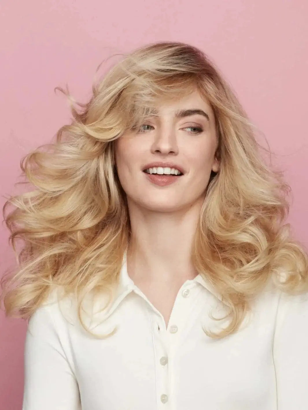 A smiling blonde model shows off a high-volume, windswept hairstyle with bounce and movement achieved using Hair by Sam McKnight Cool Girl Volume Foam | Twentyseven Toronto