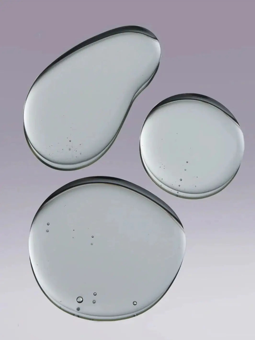 Three clear, textured droplets of gel liquid are shown against a soft purple background to represent the formula of Hair by Sam McKnight Cool Girl Volume Shampoo | Twentyseven Toronto