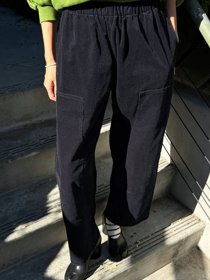 Model wearing Le Bon Shoppe Corduroy Gardener's Pants in navy with a green sweatshirt and black heels, showing the relaxed fit, elastic waist and utility pockets | Twentyseven Toronto