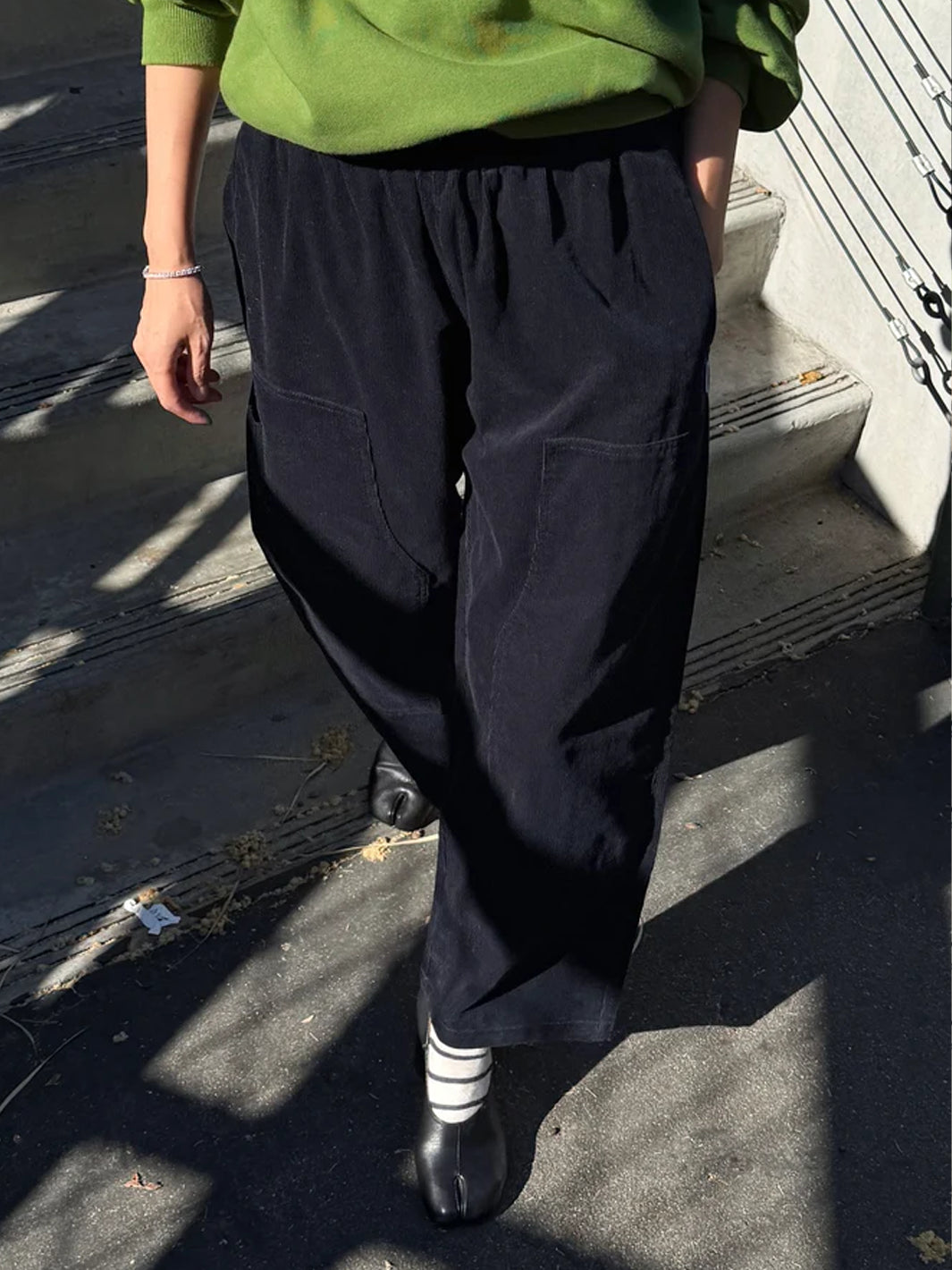 Model wearing Le Bon Shoppe Corduroy Gardener's Pants in navy with a green sweatshirt and black heels, showcasing the relaxed tapered fit and front patch pockets | Twentyseven Toronto