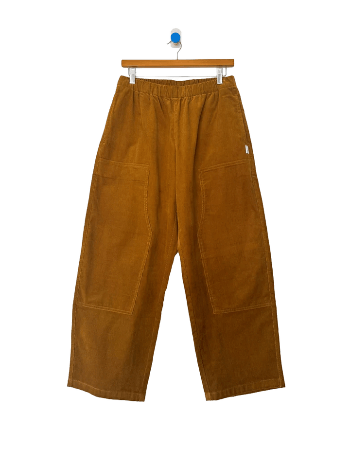 Le Bon Shoppe Corduroy Gardener's Pants in Whiskey on a wooden hanger against a white background, featuring an elastic waistband, oversized front patch pockets and relaxed tapered legs | Twentyseven Toronto