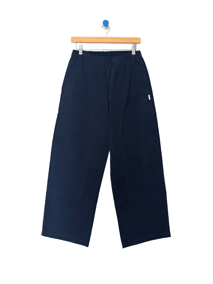 Le Bon Shoppe Corduroy Gardener's Pants in navy on a wooden hanger, featuring an elastic waistband, relaxed tapered legs and carpenter-inspired patch pockets | Twentyseven Toronto